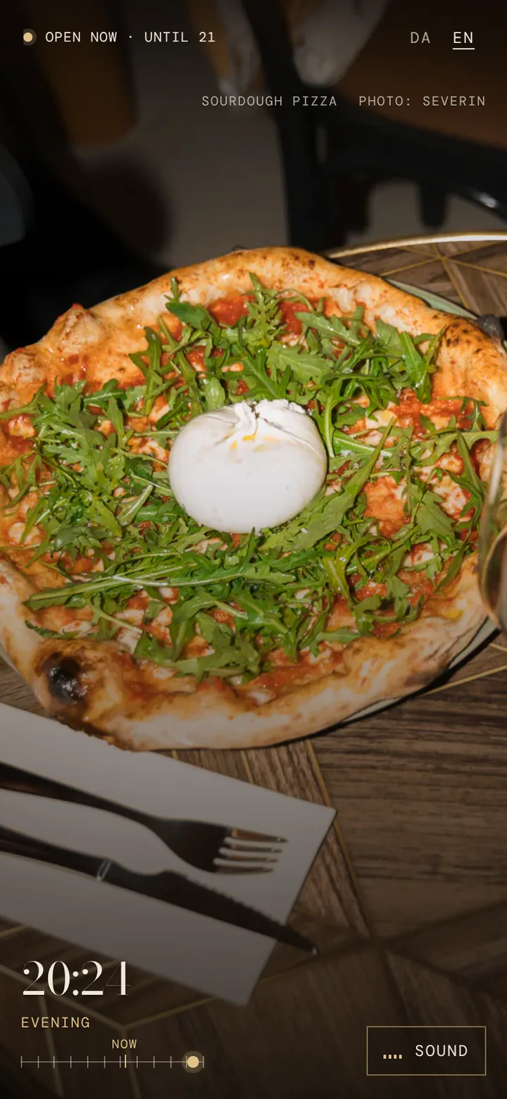 The owner's photo of a sourdough pizza with burrata and a glass of red, over the table at night.